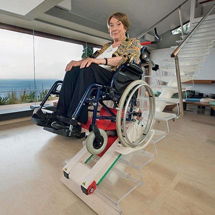 A disabled woman in a wheelchair is transported up a staircase with a wheelchair stair climber with tracks