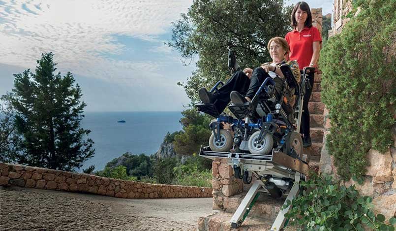 A woman in a wheelchair transported up the stairs with a tracked stair climber for wheelchair 